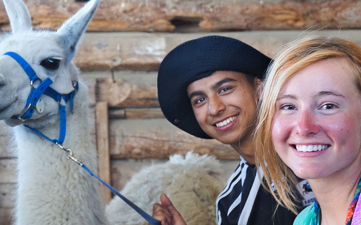 Two student smile as they pose for a photo with a llama